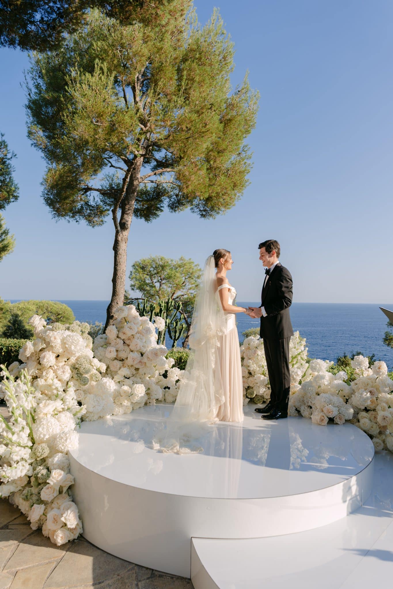 Luxury destination wedding at the Grand-Hôtel du Cap-Ferrat in Saint-Jean-Cap-Ferrat on the French Riviera, showing a white floral ceremony arrangement, a sea view aisle and a crystal draped reception pavilion.